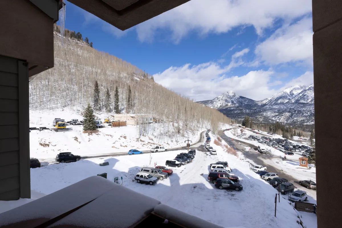 A breathtaking view of snow-capped mountains framed by elegant aspen trees, with a winding road inviting exploration through the scenic landscape. The tranquil mood and expansive natural beauty showcase the lodge’s idyllic mountain setting.