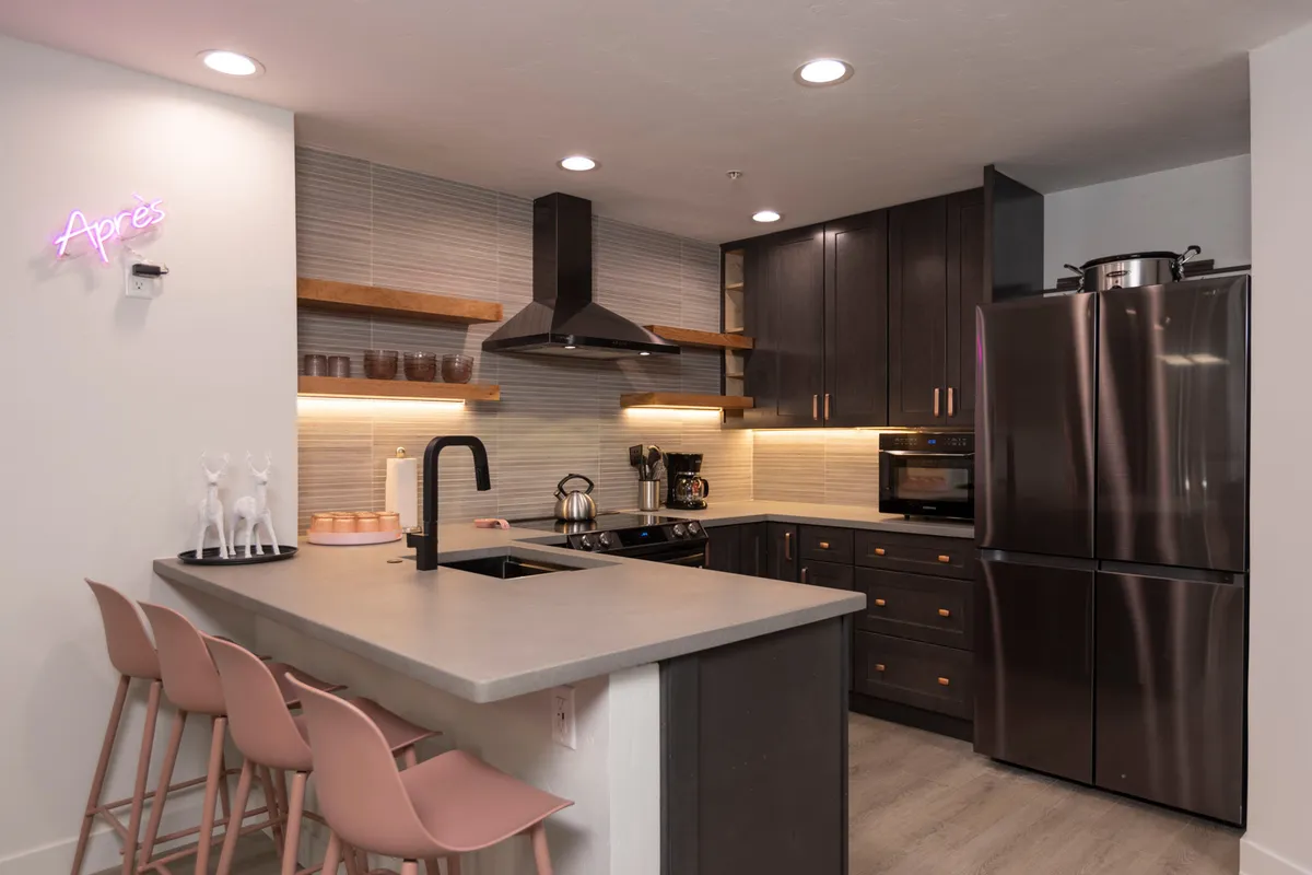 A sleek, modern kitchen with a central island, neon sign, contemporary appliances, and stylish bar stools. The open-concept design encourages socializing and culinary creativity, making it ideal for family breakfasts or après-ski feasts.