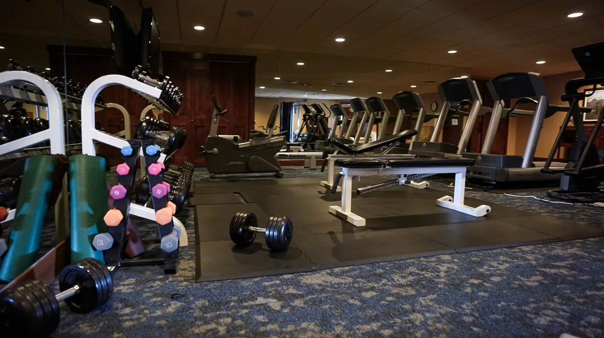 This image shows a well-equipped fitness center with treadmills, dumbbells, a weight bench, and exercise mats. The space is bright and energetic, inviting guests to maintain their wellness routines while traveling.
