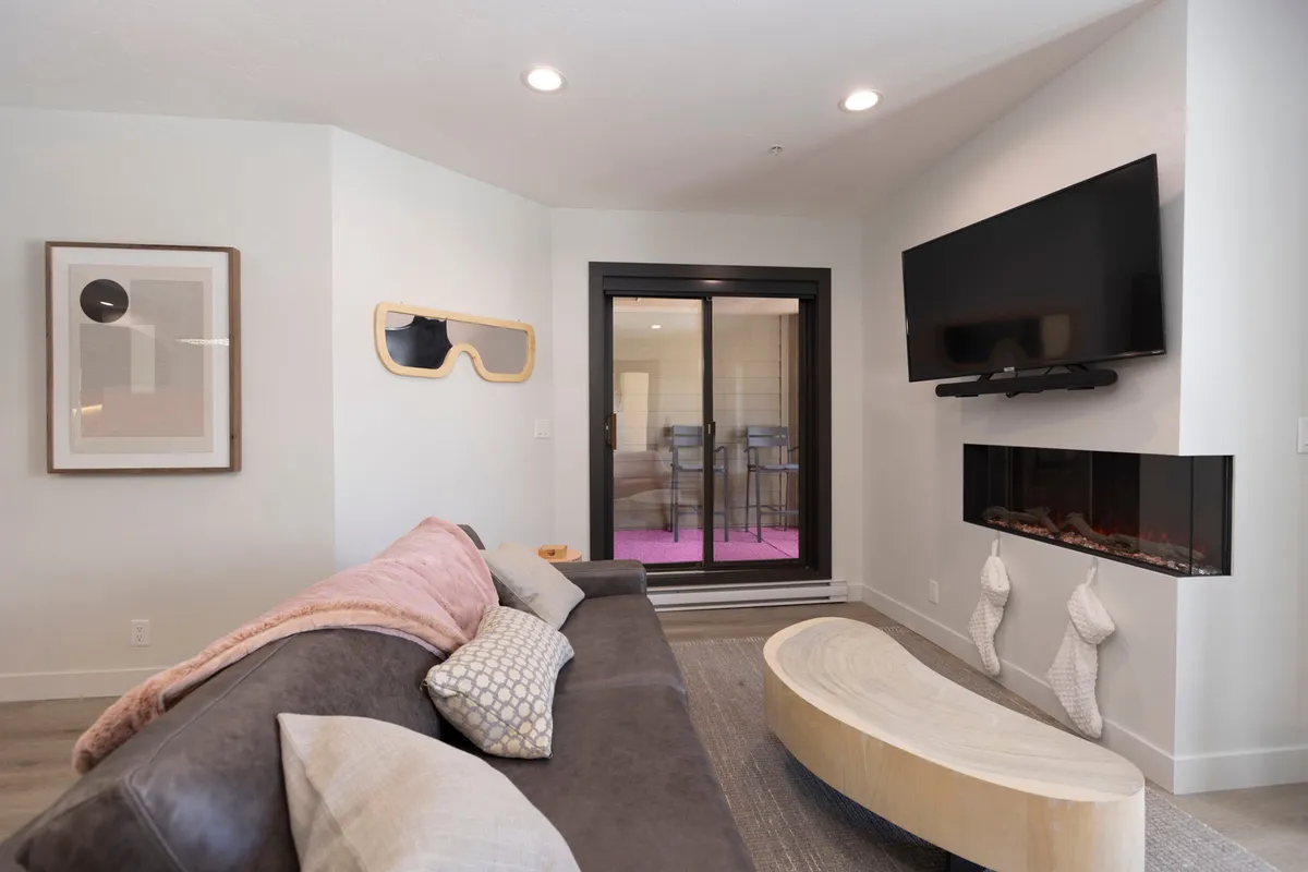 A contemporary living area with a comfortable sofa, a fireplace beneath a mounted television, tasteful artwork, and a sliding glass door that leads outside. The elements create a warm, welcoming atmosphere ideal for cozy evenings or romantic moments.